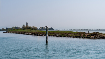 Fototapeta premium Peaceful view of Barbana Island from the water, with its iconic church and towers emerging through the lagoon’s calm reflections.