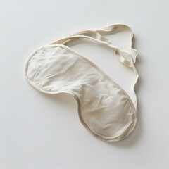 Beige eye mask made of organic cotton with soft fabric and an elastic band on a white surface illuminated by natural sunlight