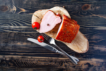 A piece of delicious pastrami made from tender meat, cutlery and cherry tomatoes as a close-up decoration on a dark wooden background