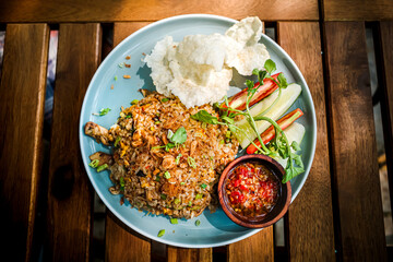 Tasty and well-known Indonesian traditional fried rice with sambal and fresh vegetables served on table at an outdoor restaurant for lunch, looking delicious and tempting