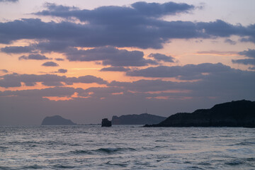 A moody spring dawn in Jinshan, Taiwan, features dark clouds drifting across an orange-tinted sky,...