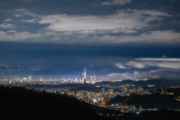 A spring evening view from Lion's Head Mountain in Xindian, Taiwan. White clouds glide above the illuminated urban skyline, creating a striking contrast against the dark night.