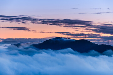 A serene spring dawn at Lion Head Mountain, Taiwan. Orange skies meet flowing white clouds, with silhouettes of power line towers.