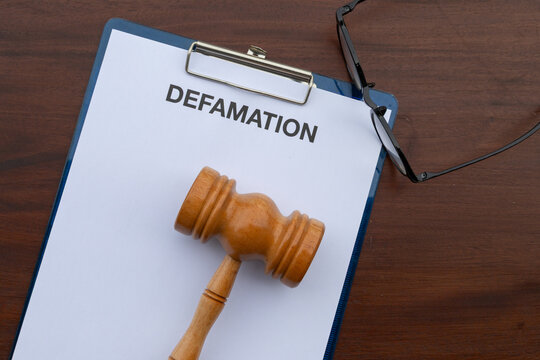 A clipboard holds a defamation legal paper next to a judge&rsquo;s gavel on a brown wooden desk, symbolizing justice in motion and legal readiness.

