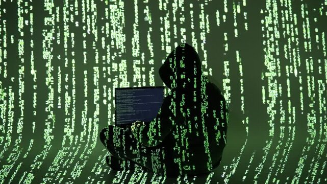 Zamaskowany haker przy laptopie w ciemnym pokoju z zielonym kodem matrix &ndash; cyberprzestępczość, cyberatak, ciemna sieć, cyberświat, kodowanie, cyfrowe zagrożenie, hakowanie systemu