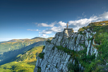 Male hiker carefully descends rocky cliff in the mountains with trekking poles, with scenic...