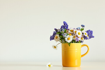 Spring flower arrangement with daisies and other wild flowers standing in a yellow cup.
