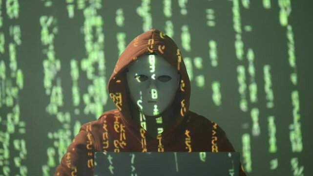 Anonimowy haker w masce z kapturem przed komputerem w ciemnym pokoju z zielonym kodem matrix, cyberprzestępstwo, bezpieczeństwo cyfrowe i cyberzagrożenia w sieci