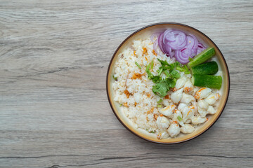 Garlic fried rice in a brown burnt ceramic plat topped with steamed crab meat, shallots and cucumber  on wooden table, Top view.