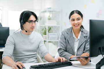 call center customer service representative wearing headset collaborates with colleague in modern office, using computer and tablet to manage CRM tasks efficiently