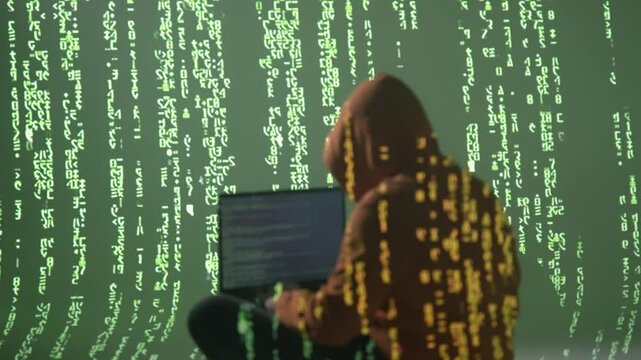 Haker w masce przy laptopie otoczony zielonym kodem matrix, cyberprzestępczość i ciemny internet, koncepcja anonimowości, cyberbezpieczeństwa i zagrożeń w cyfrowym świecie