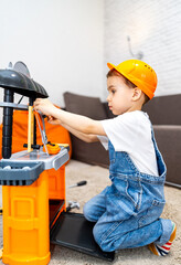 Child plays with toy tools. A boy is kneeling on the carpet, focused on assembling tools at his...
