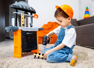 Boy plays DIY activities. A young boy with a hard hat uses a toy drill to work on a play kitchen...