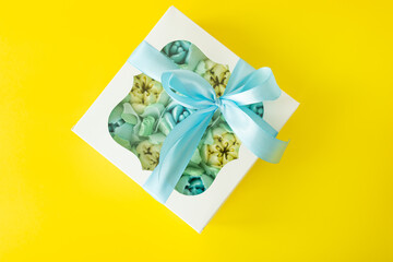White gift box with pastel blue sweets inside, tied with a blue ribbon on a yellow background.