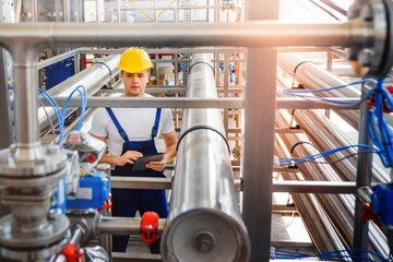 Young engineer worker doing inspection work with tablet computer at modern chemical factory among...