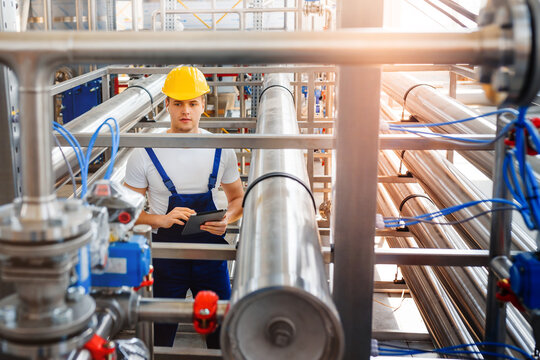 Young engineer worker doing inspection work with tablet computer at modern chemical factory among pipelines.