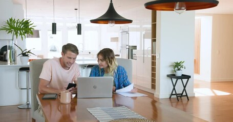 Couple celebrating success at home, joyfully waving papers near laptop