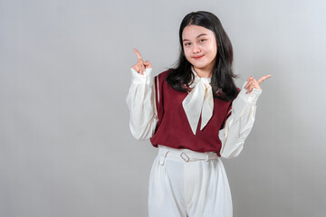 Smiling young Asian woman pointing both index fingers upward with a confident and playful...