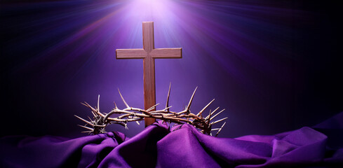 Una cruz de madera iluminada con luz divina con una corona de espinas sobre una túnica morada representado la pasión y crucifixión de Jesucristo en Semana Santa © theshooter