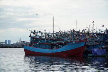 Fototapeta premium Colorful Fishing Boats Moored at Harbor with Calm Water and Overcast Sky in Coastal City