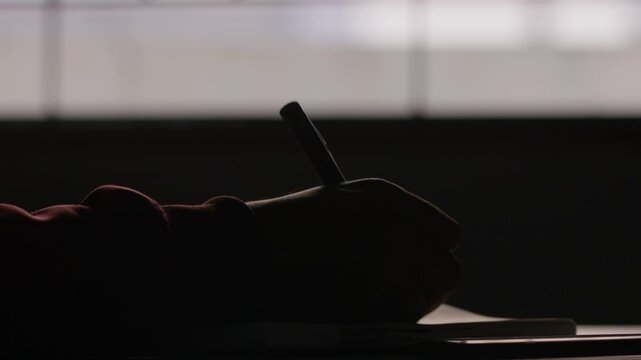 A closeup slow-motion dimly lit scene of a hand is writing, leaving the pen and picking phone, started to scroll