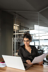 Smiling latin or arabian young business woman hr working on laptop computer reading finance...