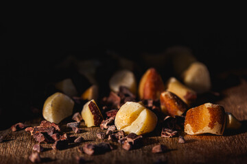 Chopped Brazil nuts and cacao nibs lie scattered across a wooden table, lit by directional light...