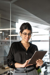 Young indian or arabian arab woman ceo manager holding digital computer tab for business project. Middle eastern or latin businesswoman using tablet pc online app for work standing in office. Vertical