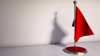 Vibrant red table flag standing proudly on a reflective surface casting shadow against a blank wall in a minimalist setting.