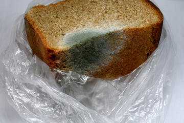 Moldy rye bread in close-up on a light background. Bread, unsuitable for food. Mold due to improper storage of the product. Mold stains on bread. Selective focus.