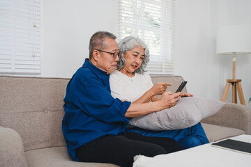 Obraz premium Senior couple enjoying pensionretirement while using smartphone together on cozy sofa in bright living room