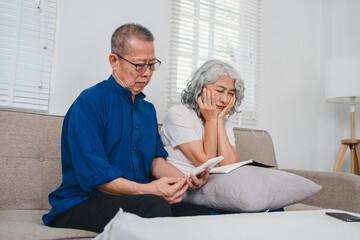 Obraz premium Elderly couple sitting on sofa, reading and reflecting on pension and retirement plans in cozy living room setting