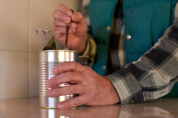 Worker's hands gripping metal can and spoon, scooping prepared meal during kitchen lunch break, depicting simple dining moment