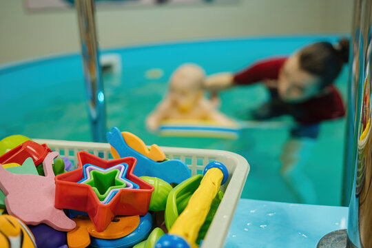 Plastic toys for babies. Newborn baby learns to swim in pool water, female coach