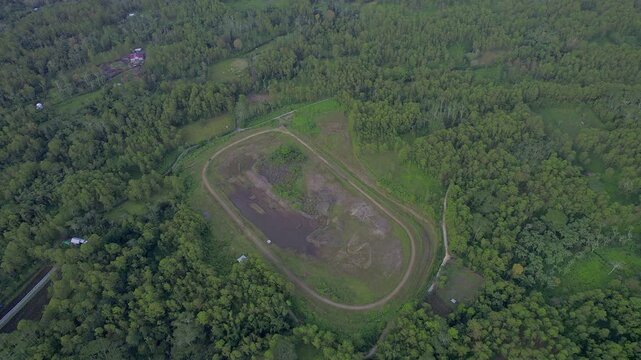 Aerial footage of a motocross racing track nestled in a forest, showcasing sections flooded from heavy rainfall. Ideal for themes like extreme sports, weather impact, and forest terrain.