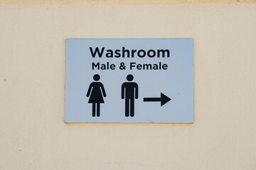 A clear and straightforward washroom sign indicating male and female facilities with a directional arrow. The sign features simple iconography on a light-colored background for easy visibility