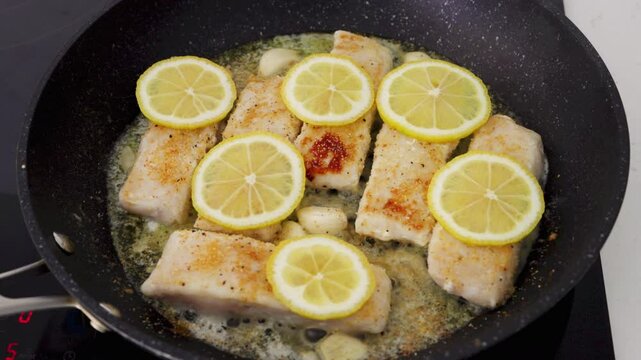  Hake fillets cook in a pan with garlic, lemon slices, and a buttery sauce. High quality 4k footage