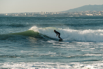 surfer surfing in the sea, portugal, costa de caparica, city in the background