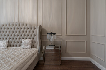 bedroom design with a double bed, large upholstered headboard. the lamp on the bedside table. a lamp with crystals. elegant interior. a photo of a bedroom in beige shades.