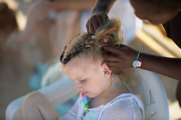holding braids with pink color on little kid head. stylist applying braiding hair on young baby.