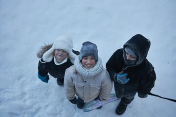 Three young children, bundled up from head to toe in warm winter gear, beam with pure delight as they gather together for a picture amidst a pristine snowy mountain backdrop.