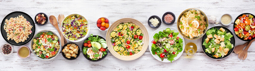 Assortment of delicious homemade salads. Above view table scene on a white wood banner background....