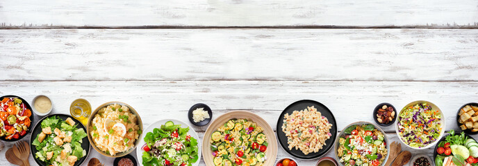 Variety of delicious homemade salads. Top down view bottom border on a white wood banner background. Summer food concept. Potato, caesar, pasta and green salads.