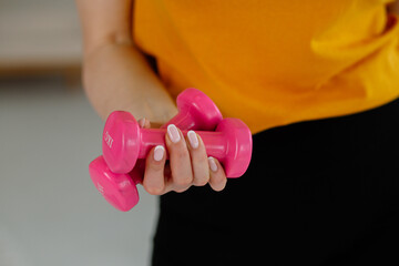 Hand holding pink dumbbells, strength and fitnes. Close-up of pink dumbbells in woman’s hand during home workout
