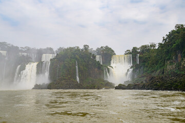 There is a beautiful waterfall located right in the center of a wide river, and it is elegantly surrounded by lush green trees
