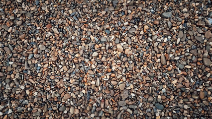 Multicolored wet pebbles texture with rocks varying in size and shapes. Natural arrangement highlights earthy tones like tan, gray, and brown. Smooth and rough surfaces create an intricate pattern