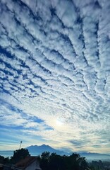 A stunning sky filled with textured clouds stretches above distant mountains, glowing softly with...