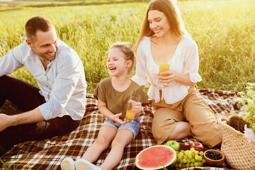 Eating Outdoors. Happy parents and excited baby resting and sitting on grass, drinking orange juice, enjoying the day