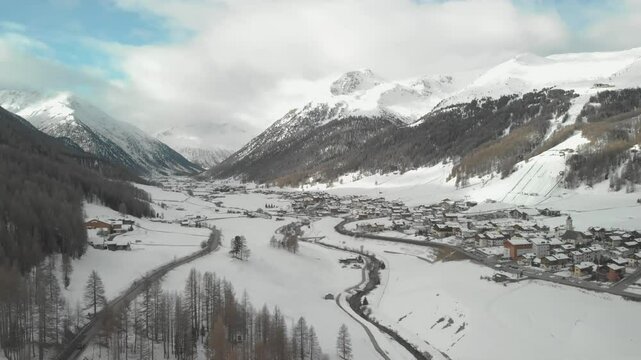 Panoramic drone view of the beautiful Livigno valley surrounded by snow-capped Alps during a cloudy winter day. Livigno is one of the venues of the next Winter Olympic Games.