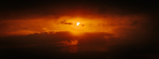 A partial solar eclipse glows through dramatic red-orange clouds, casting an intense and surreal light in a dark sky. Includes ample copy space.